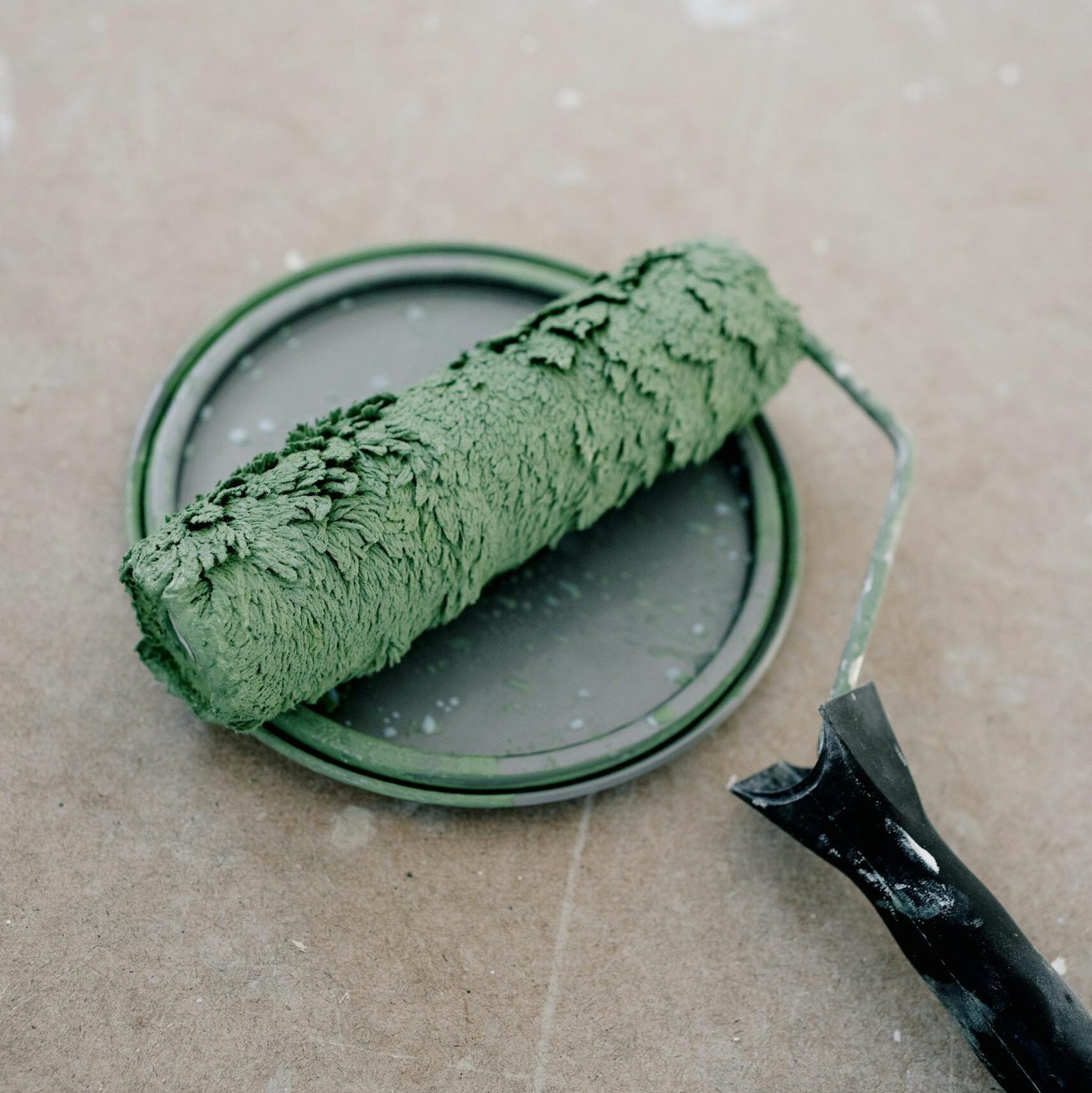 From above of dirty paint roller on green plastic cap on cement floor during repair